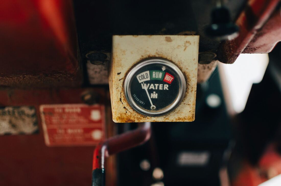 A weathered temperature gauge on a vintage tractor, marked cold, run and hot, with the needle resting between them.